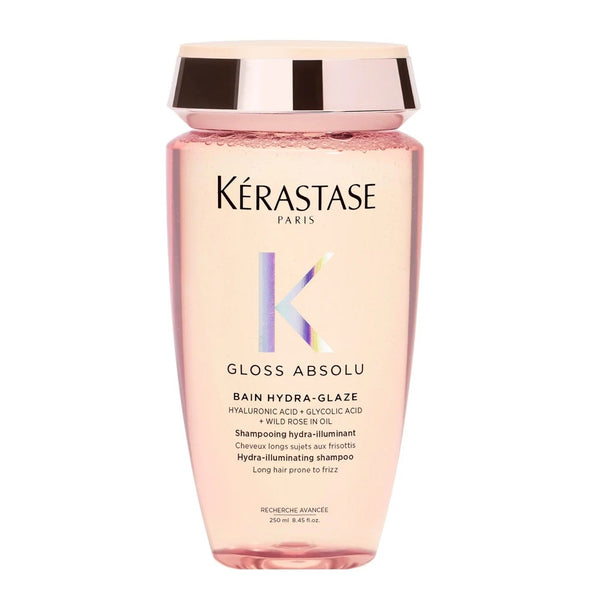 A clear glass bottle of Kerastase Gloss Absolu Bain Hydra-Glaze Shampoo with a pink label and a silver cap.
