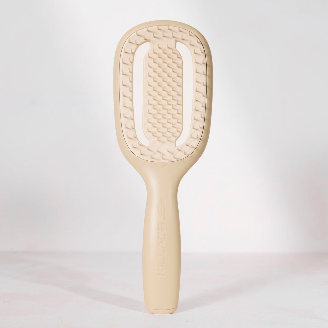 A single beige hairbrush with a textured paddle head and smooth handle, photographed upright against a clean white studio background.