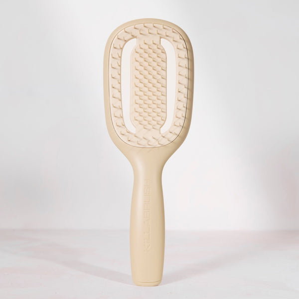 A single beige hairbrush with a textured paddle head and smooth handle, photographed upright against a clean white studio background.