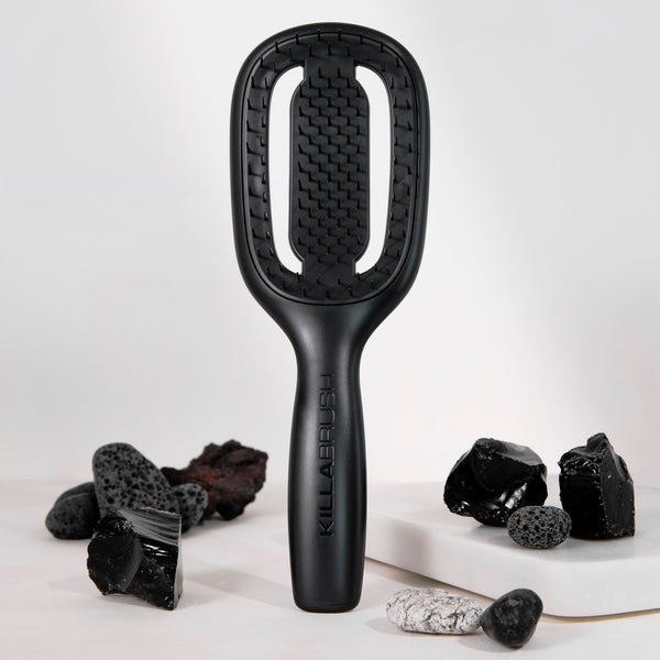 A black hairbrush with a textured, honeycomb-like bristle head and a matte handle, standing upright on a white surface. The brand name 'GILLABEET' is printed vertically on the handle.