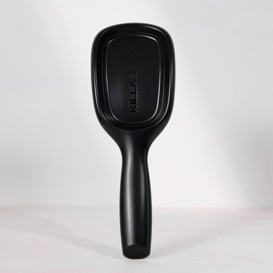 A matte black KiraBell paddle hairbrush standing upright against a clean white studio background.