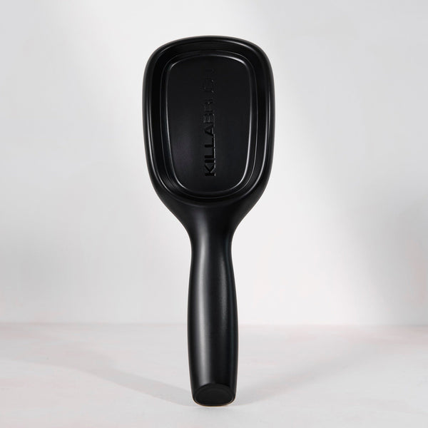 A matte black KiraBell paddle hairbrush standing upright against a clean white studio background.