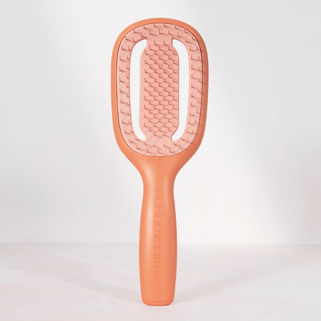 A peach-colored hairbrush with a textured bristle head and a smooth handle, standing upright against a clean white background.