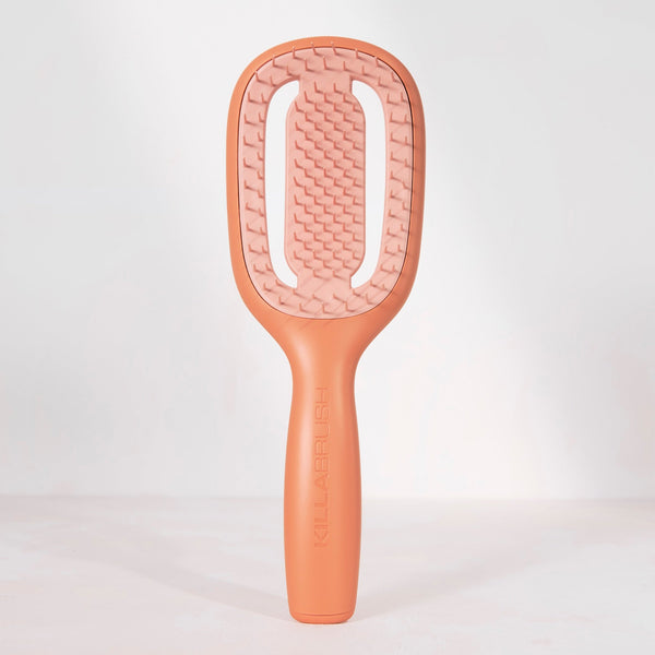 A peach-colored hairbrush with a textured bristle head and a smooth handle, standing upright against a clean white background.