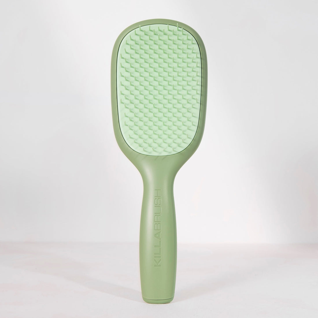 A light green hairbrush with a textured oval head and a smooth handle, standing upright against a clean white background.