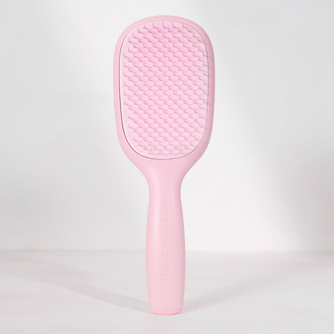 A light pink hairbrush with a textured oval head and a smooth handle, standing upright against a clean white background.