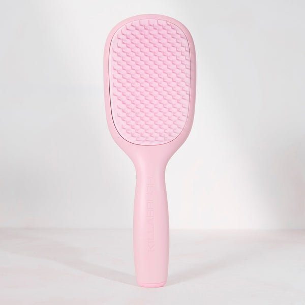 A light pink hairbrush with a textured oval head and a smooth handle, standing upright against a clean white background.