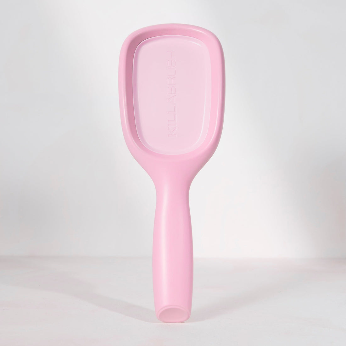 A light pink handheld plastic mirror with a handle, standing upright against a white studio background.