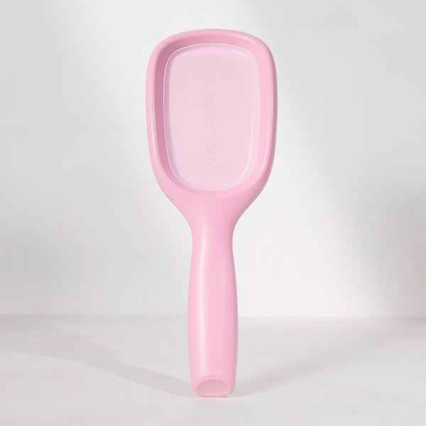 A light pink handheld plastic mirror with a handle, standing upright against a white studio background.