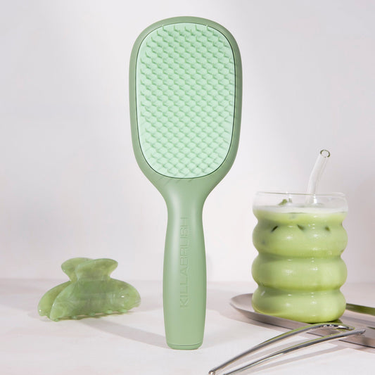 Green hairbrush next to a glass of green liquid on a white background