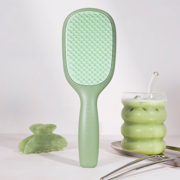 Green hairbrush next to a glass of green liquid on a white background