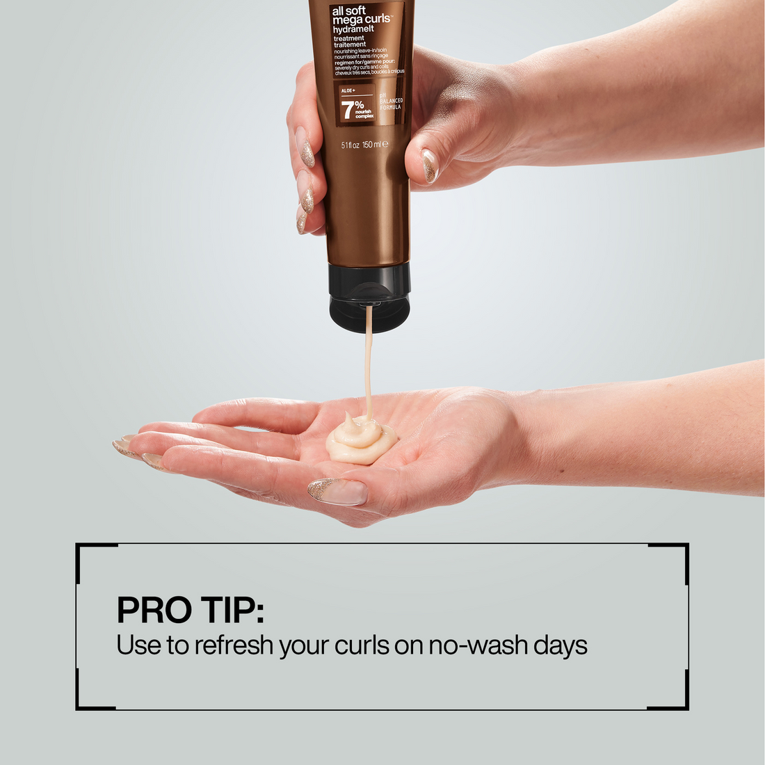 Hand holding a bottle of hair product with a small amount on a palm, against a light gray background.