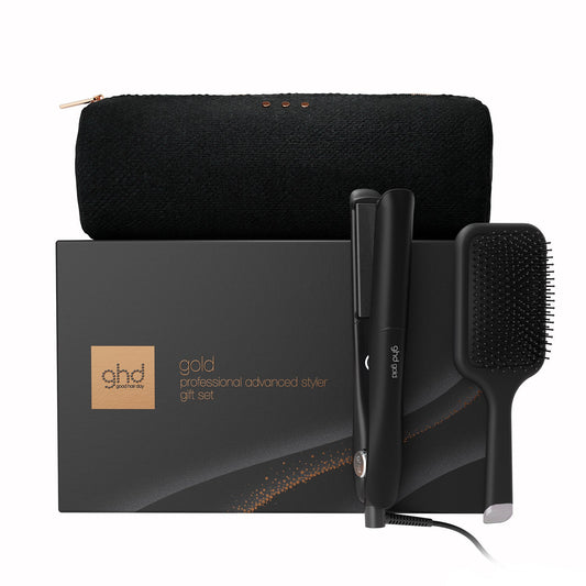 GHD gold professional advanced stylist gift set featuring a black hair dryer, flat iron, hairbrush, and black zippered pouch, arranged in front of the branded black gift box on a white background.